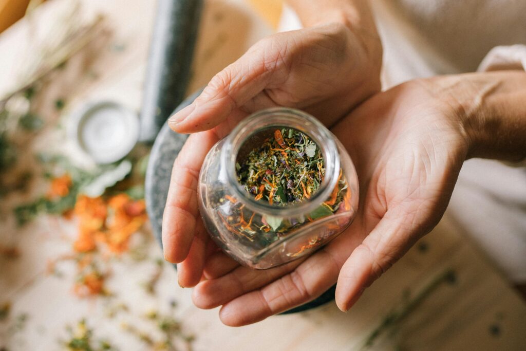 zipwp image 5480234 Close-up of hands holding a glass jar filled with colorful dried herbs.